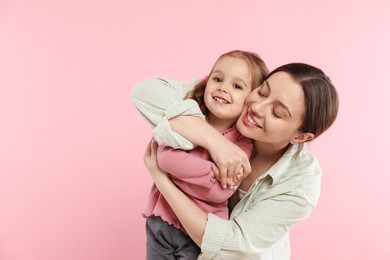 Portrait of happy mother and her cute daughter on pink background. Space for text