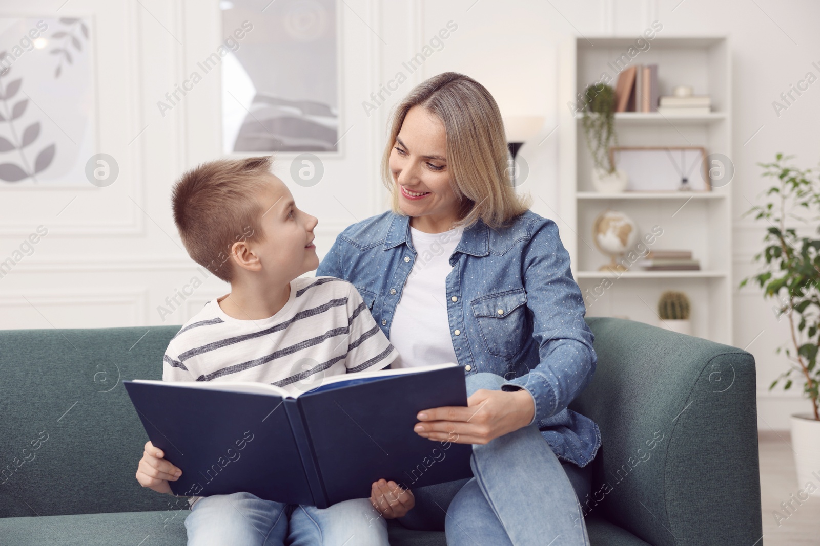 Photo of Mother and son reading book on sofa at home