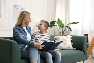 Photo of Mother and son reading book on sofa at home