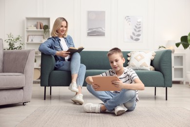 Photo of Son using tablet while his mother reading book at home, selective focus