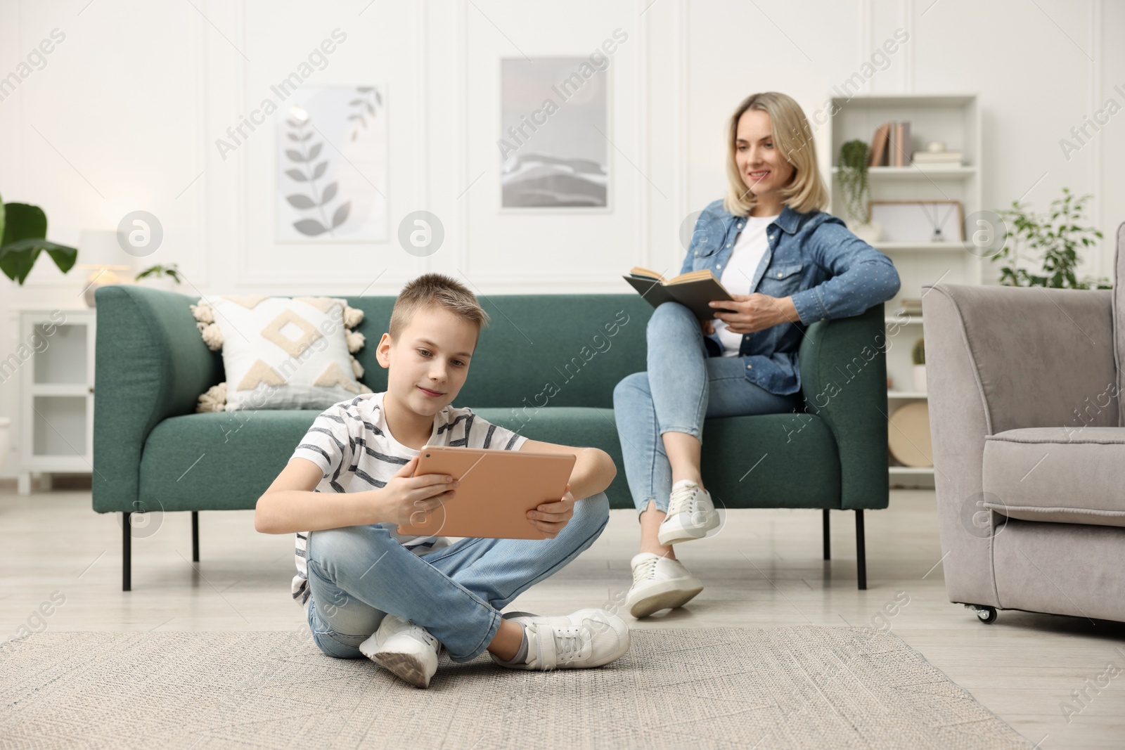 Photo of Son using tablet while his mother reading book at home, selective focus