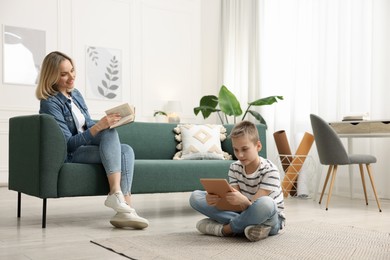 Photo of Son using tablet while his mother reading book at home