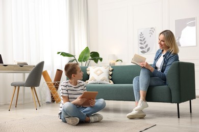 Photo of Son using tablet while his mother reading book at home