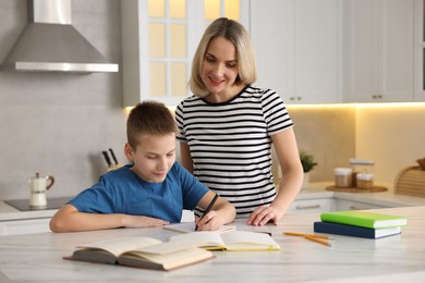 Photo of Mother and son doing homework at table indoors