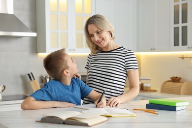 Photo of Mother and son doing homework at table indoors