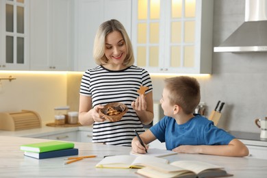 Photo of Mother and son eating cookies while doing homework indoors