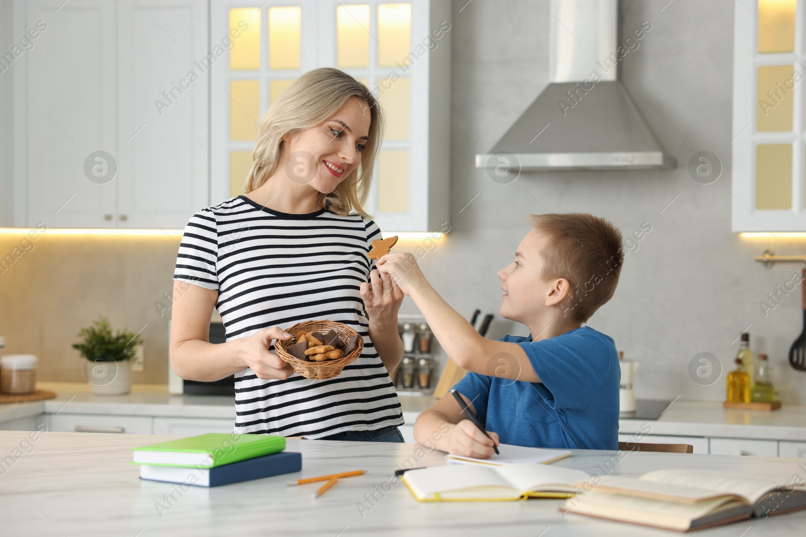 Photo of Mother and son eating cookies while doing homework indoors