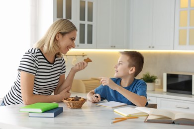 Photo of Mother and son eating cookies while doing homework indoors