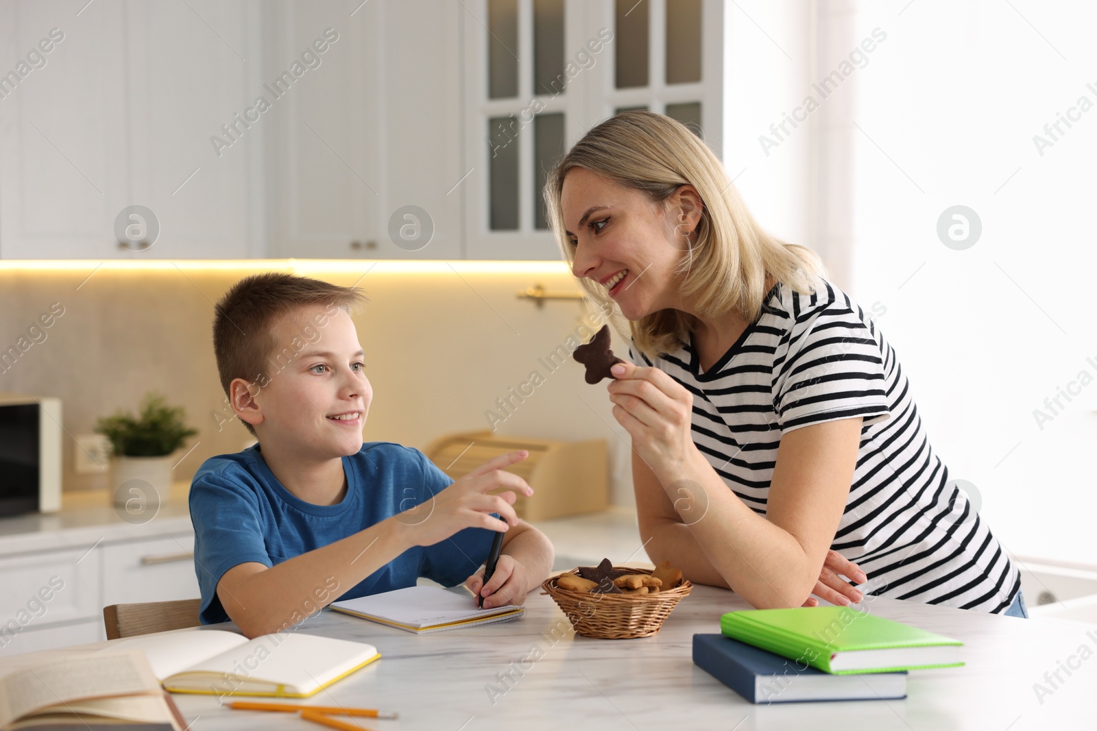 Photo of Mother and son eating cookies while doing homework indoors