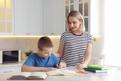 Photo of Mother and son doing homework at table indoors