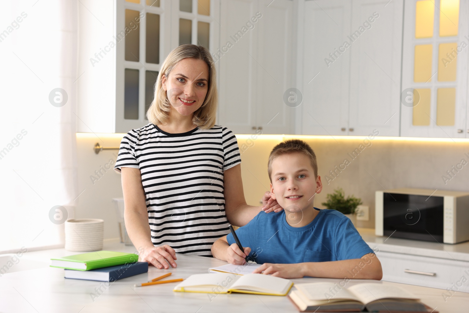 Photo of Mother and son doing homework at table indoors