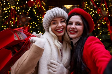 Photo of Happy friends with shopping bags taking selfie on city street. Christmas season