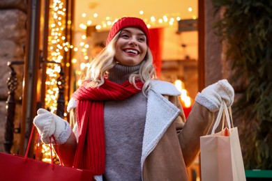 Photo of Happy woman with shopping bags on city street. Christmas season