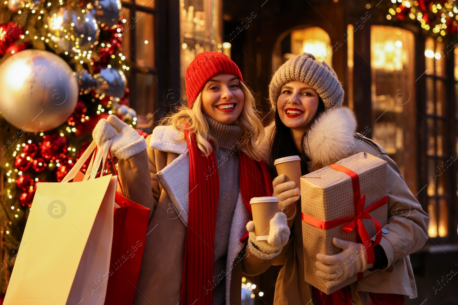 Photo of Happy friends with paper cups of coffee and Christmas gift near shop outdoors