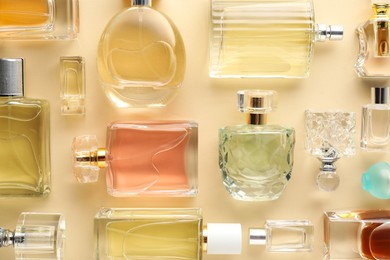 Photo of Bottles of various perfumes on beige background, flat lay