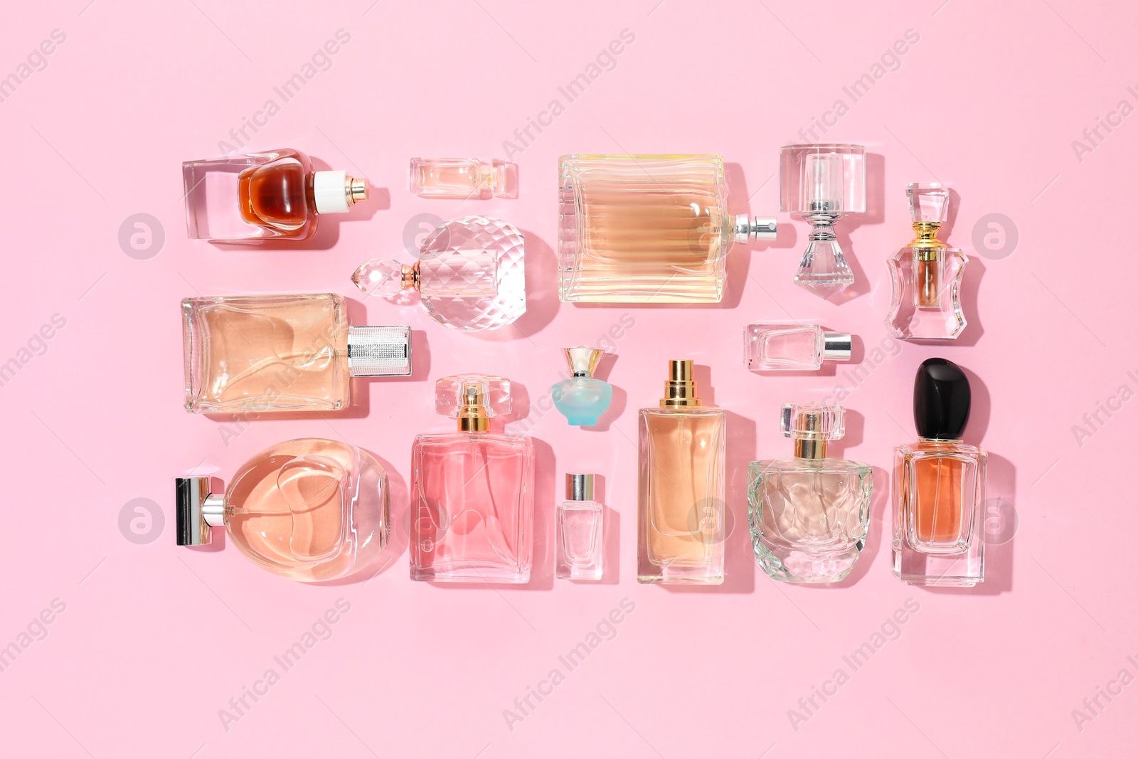 Bottles of various perfumes on pink background, flat lay Photo of Bottles of various perfumes on pink background, flat lay