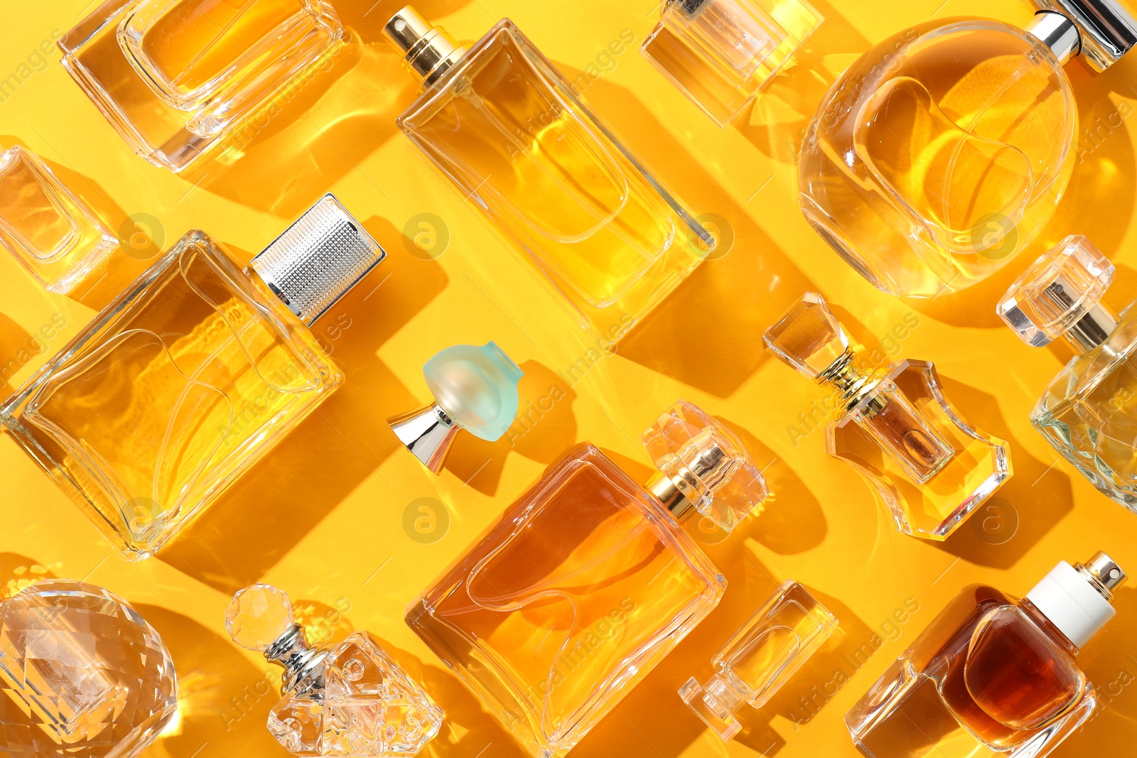 Bottles of various perfumes on yellow background, flat lay Photo of Bottles of various perfumes on yellow background, flat lay