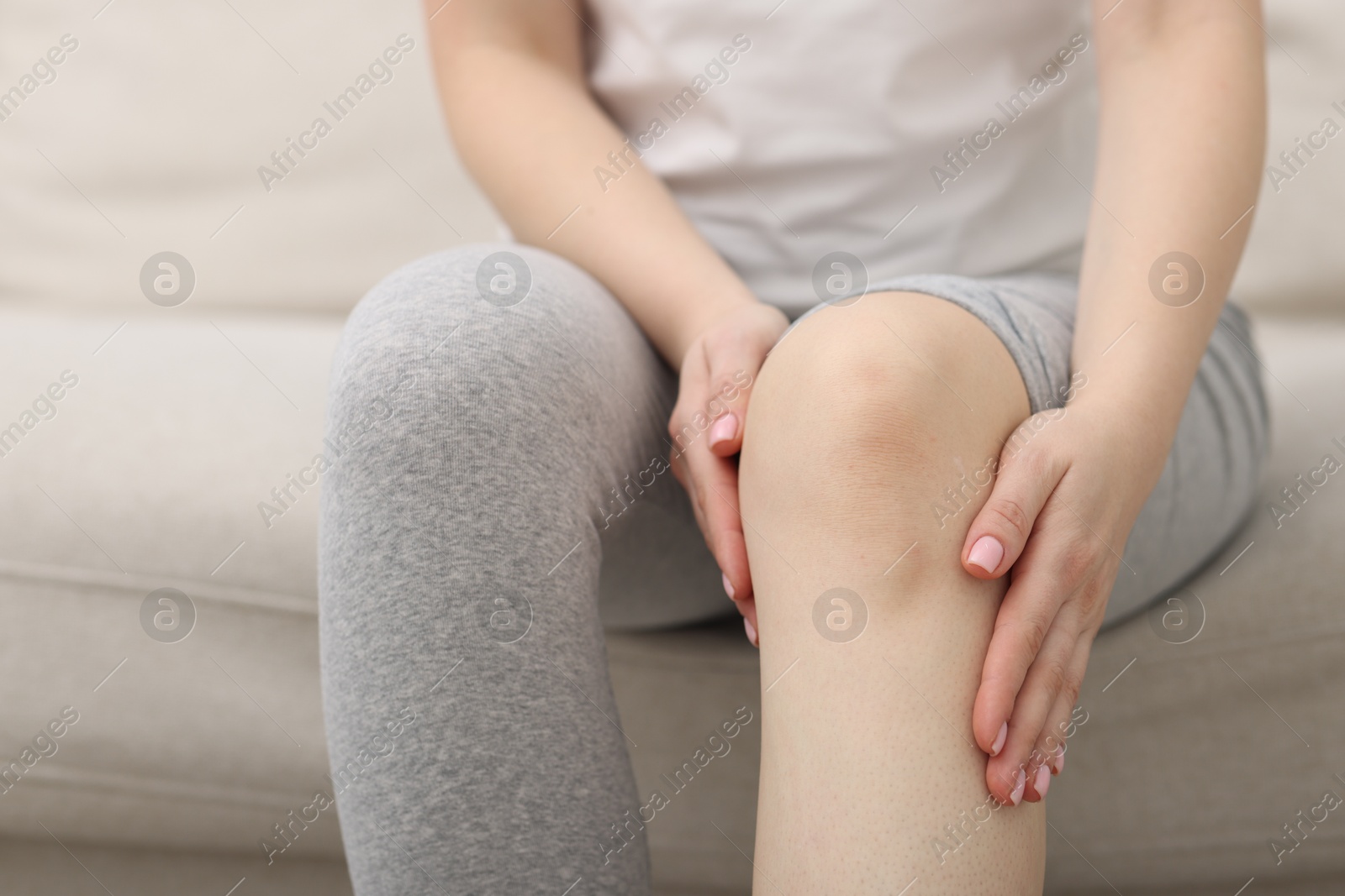 Photo of Young woman suffering from pain in knee on sofa at home, closeup