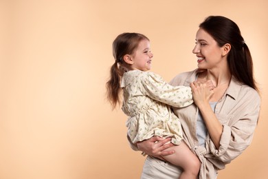 Happy mother with her cute little daughter on beige background, space for text