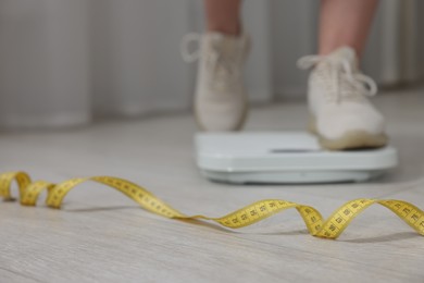 Photo of Woman on scales and measuring tape on floor indoors, selective focus. Weight loss