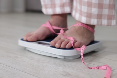 Photo of Woman on scales and measuring tape indoors, closeup. Weight loss