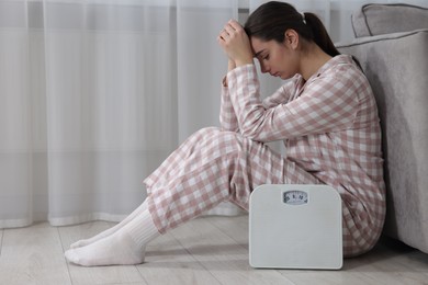 Photo of Depressed woman with scales on floor at home, space for text. Bulimia problem