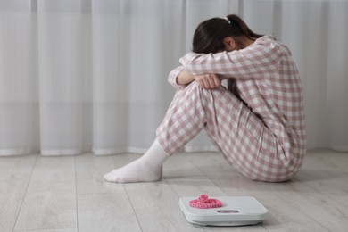 Photo of Depressed woman, scales and measuring tape on floor at home, selective focus with space for text. Bulimia problem