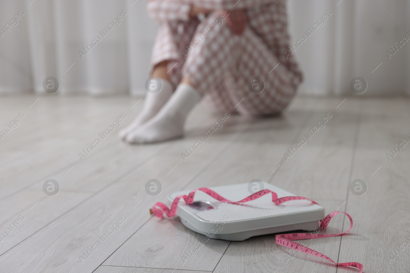 Photo of Depressed woman and scales with measuring tape on floor at home, selective focus. Bulimia problem