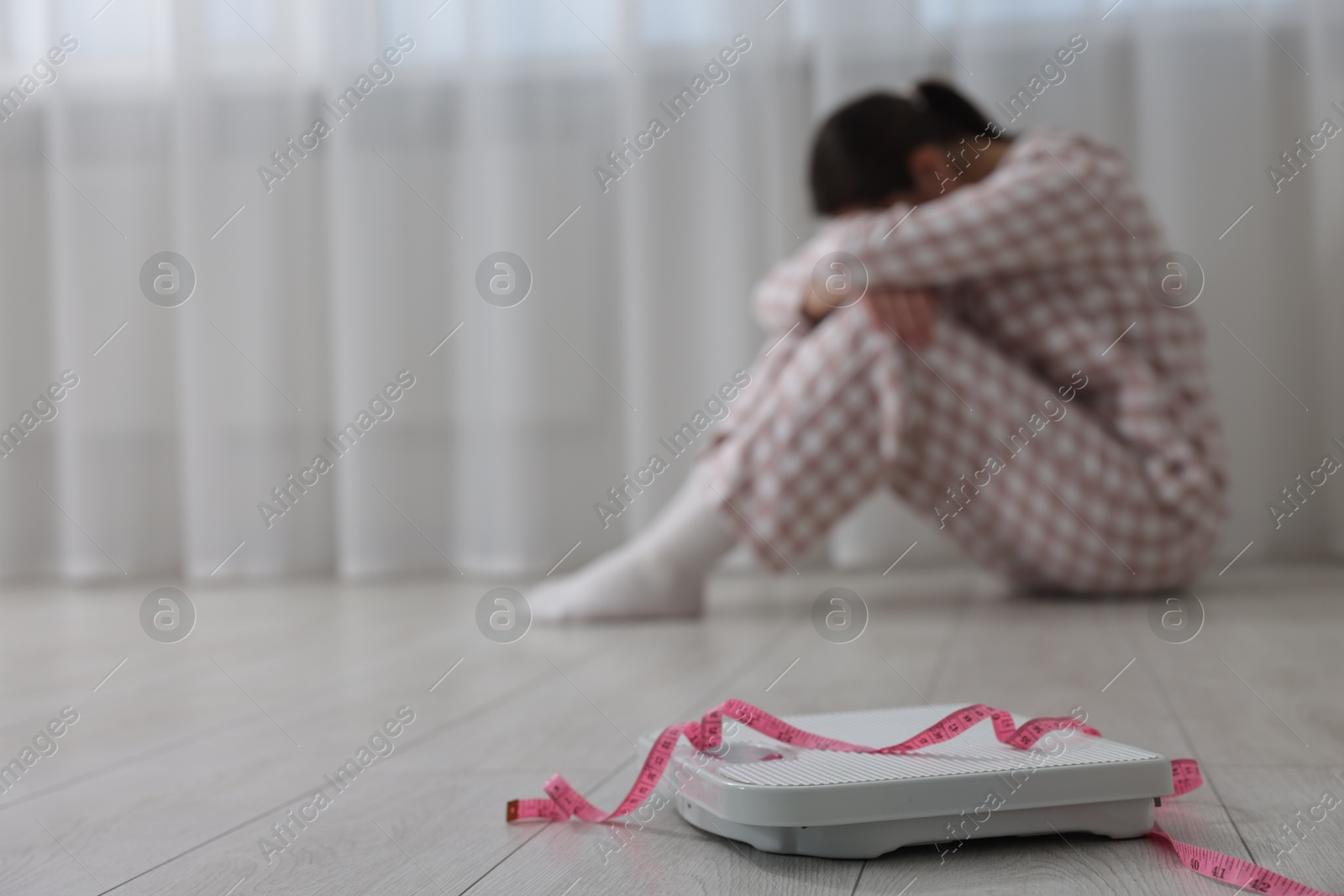 Photo of Depressed woman, scales and measuring tape on floor at home, selective focus with space for text. Bulimia problem