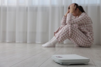 Photo of Depressed woman and scales on floor at home, selective focus with space for text. Bulimia problem