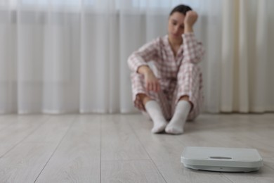 Photo of Depressed woman and scales on floor at home, selective focus with space for text. Bulimia problem