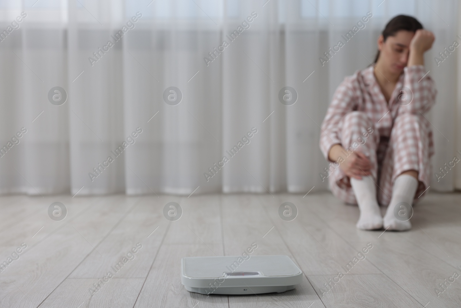 Photo of Depressed woman and scales on floor at home, selective focus with space for text. Bulimia problem