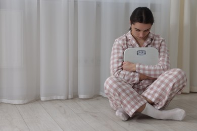 Photo of Depressed woman with scales on floor at home, space for text. Bulimia problem