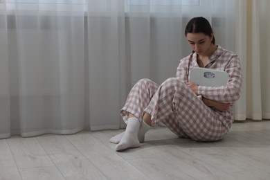 Photo of Depressed woman with scales on floor at home, space for text. Bulimia problem