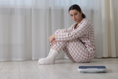 Photo of Depressed woman with scales on floor at home, space for text. Bulimia problem