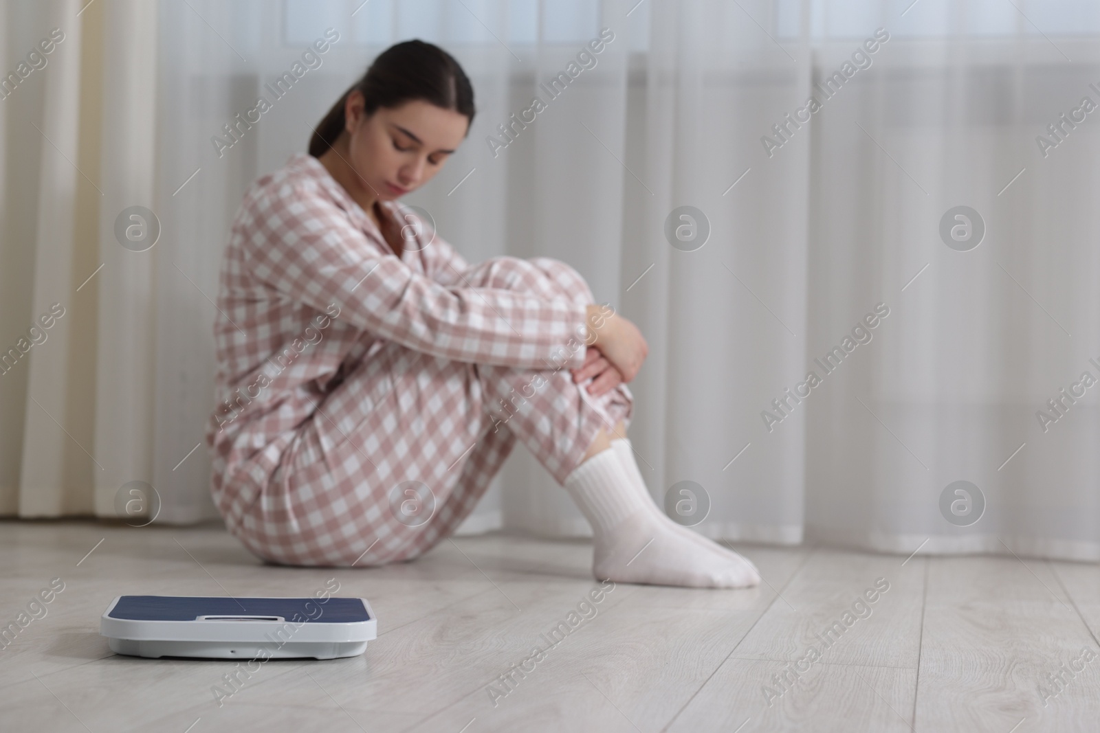 Photo of Depressed woman with scales on floor at home, space for text. Bulimia problem