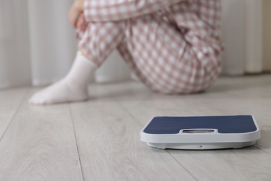 Photo of Depressed woman and scales on floor at home, selective focus. Bulimia problem