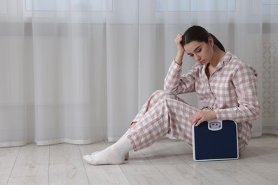 Photo of Depressed woman with scales on floor at home, space for text. Bulimia problem