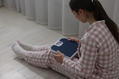 Photo of Depressed woman with scales on floor at home. Bulimia problem