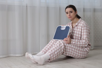 Photo of Depressed woman with scales on floor at home, space for text. Bulimia problem