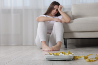 Photo of Depressed woman, scales and measuring tape on floor at home, selective focus with space for text. Bulimia problem