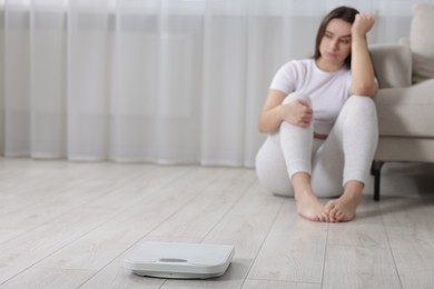 Photo of Depressed woman and scales on floor at home, selective focus with space for text. Bulimia problem