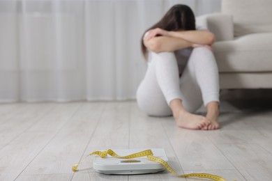 Photo of Depressed woman, scales and measuring tape on floor at home, selective focus with space for text. Bulimia problem