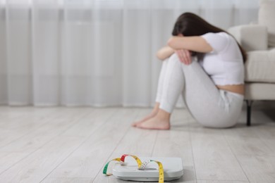 Photo of Depressed woman, scales and measuring tape on floor at home, selective focus with space for text. Bulimia problem