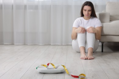 Photo of Depressed woman, scales and measuring tape on floor at home, selective focus with space for text. Bulimia problem