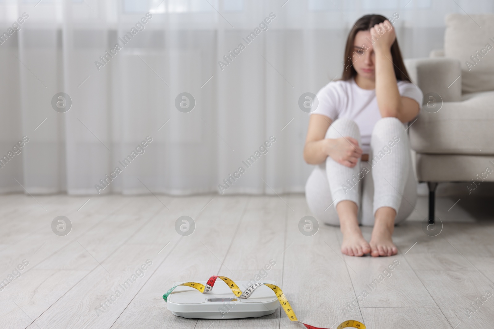 Photo of Depressed woman, scales and measuring tape on floor at home, selective focus with space for text. Bulimia problem