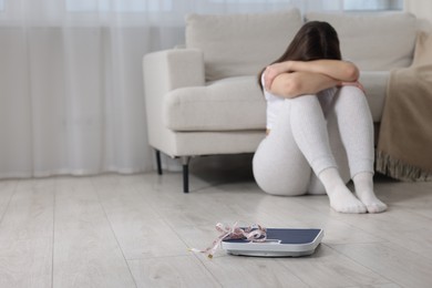 Photo of Depressed woman, scales and measuring tape on floor at home, selective focus with space for text. Bulimia problem