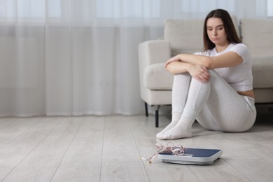 Photo of Depressed woman, scales and measuring tape on floor at home, selective focus with space for text. Bulimia problem