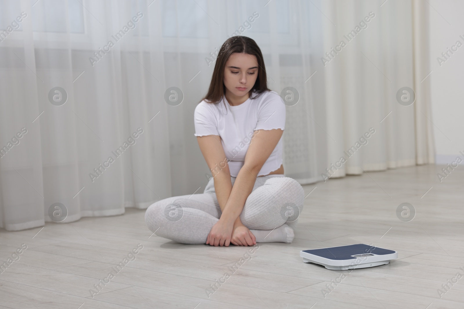 Photo of Depressed woman with scales on floor at home. Bulimia problem