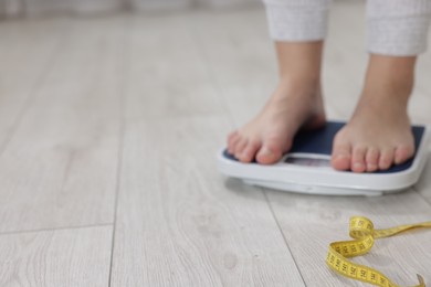 Photo of Woman on scales and measuring tape on floor indoors, selective focus with space for text. Weight loss